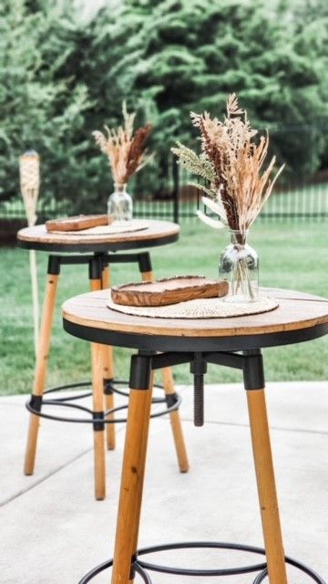 Two tables with vases of dried flowers on them are sitting on a patio.