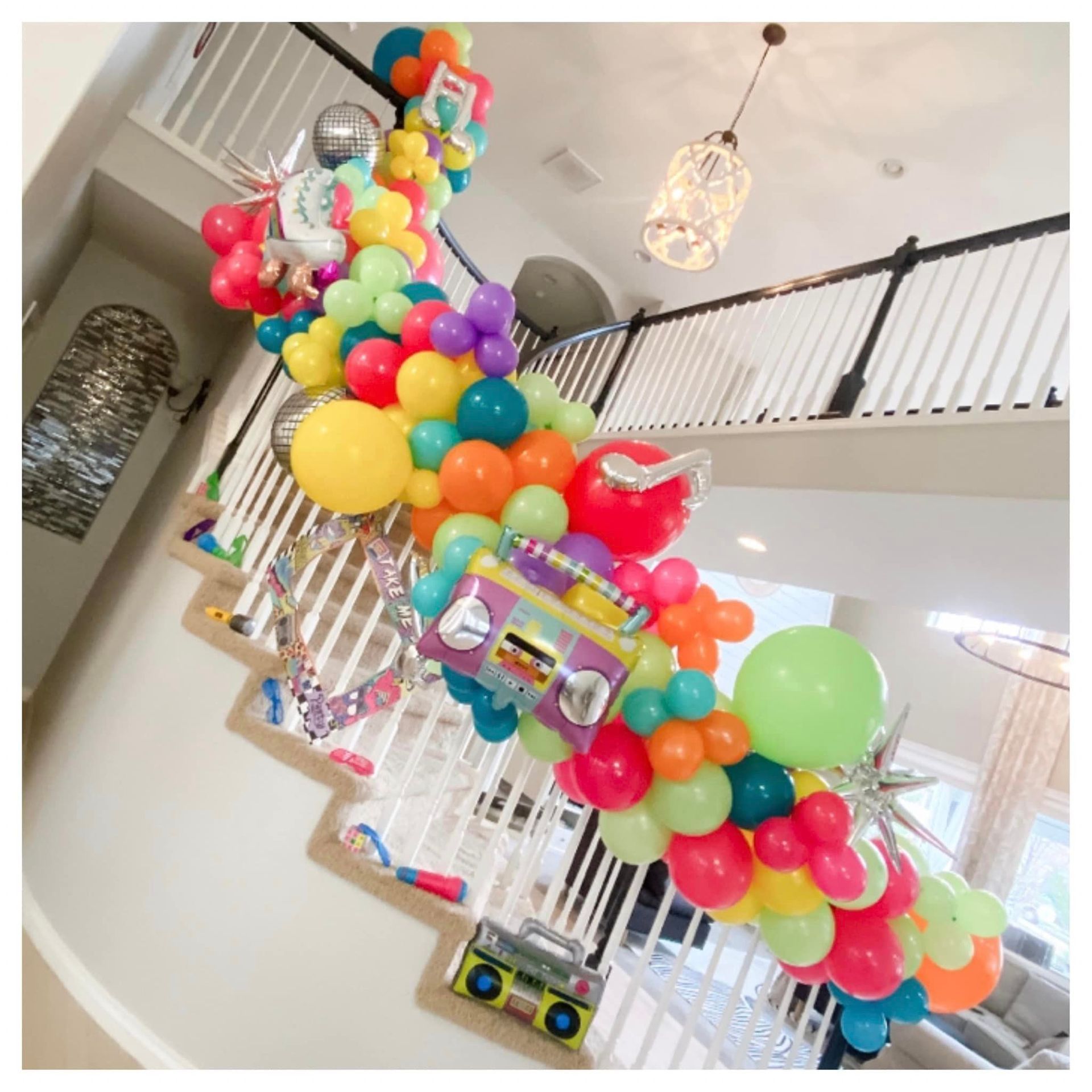 A bunch of colorful balloons are hanging from the ceiling of a staircase.