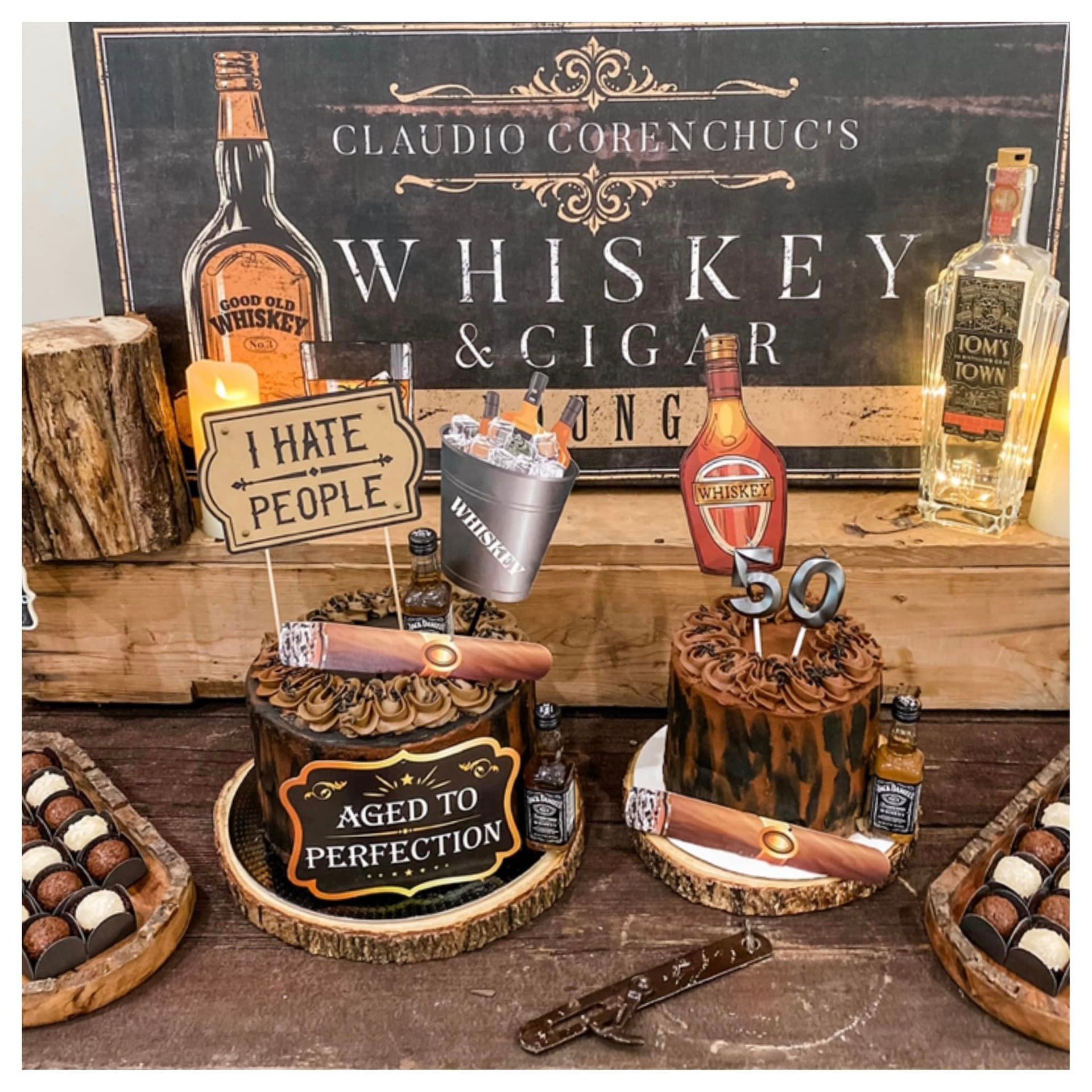 A wooden table topped with cakes and bottles of whiskey and cigars.