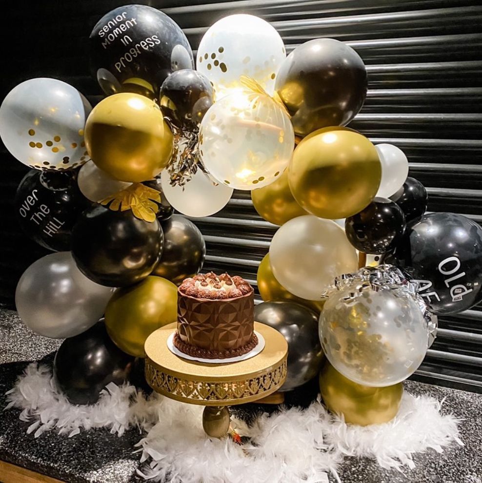 A cake on a cake stand surrounded by balloons.