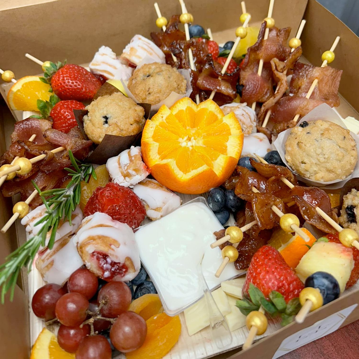 A box filled with a variety of food and fruit on skewers.