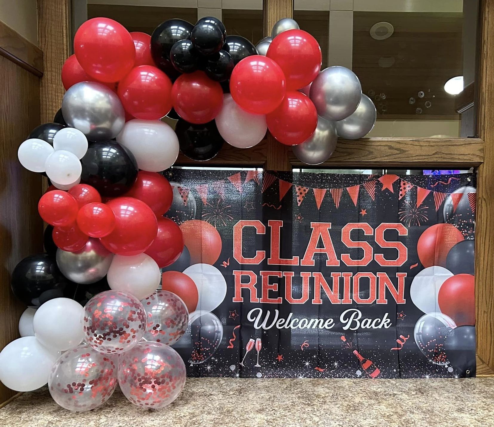 A bunch of balloons are sitting in front of a sign that says class reunion welcome back.