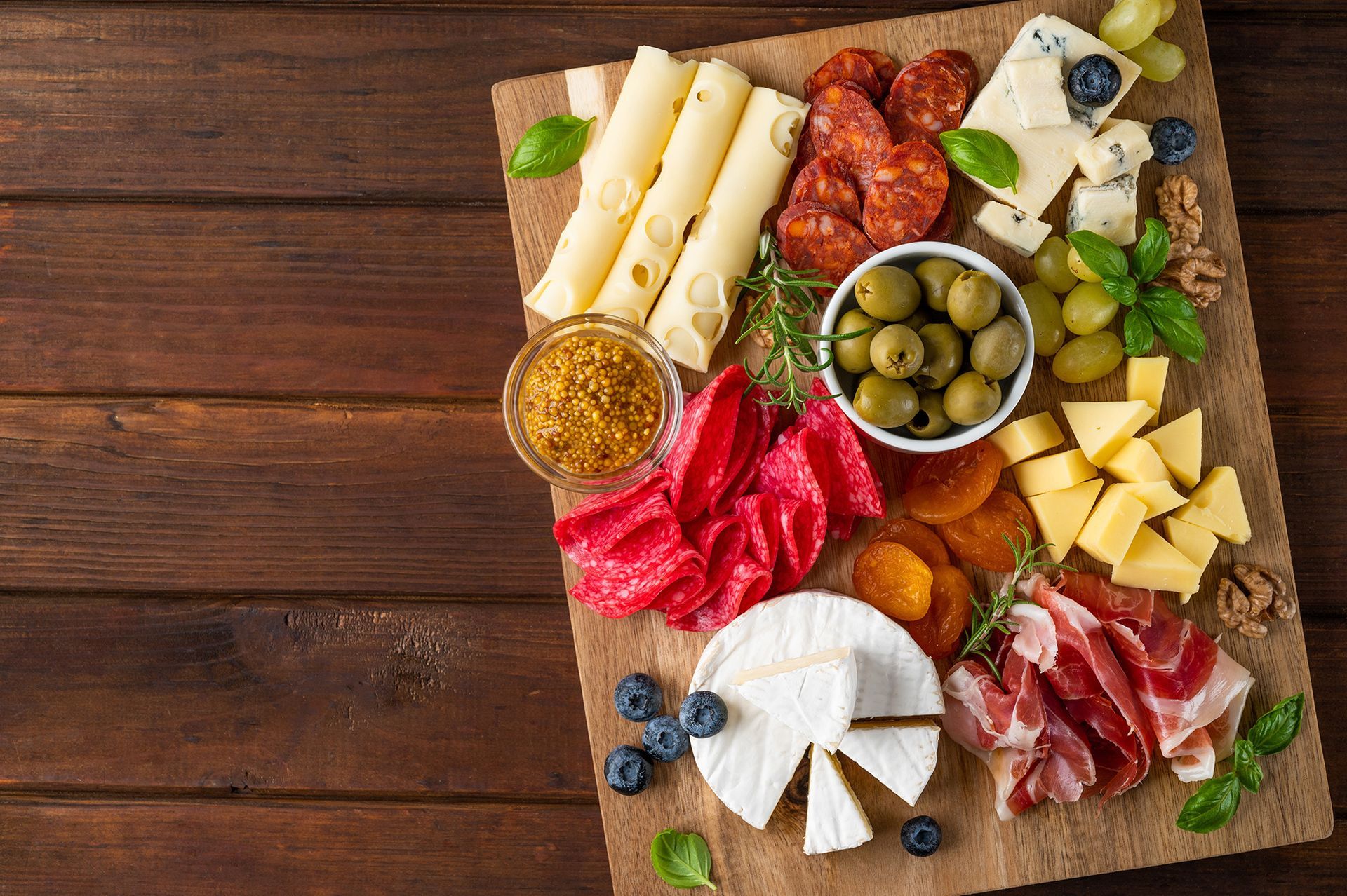 A wooden cutting board topped with a variety of cheeses , meats and olives.