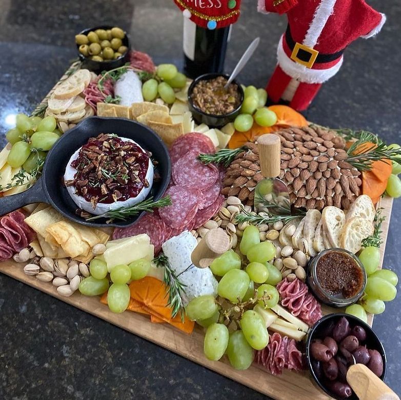 A wooden cutting board filled with lots of food including grapes and nuts