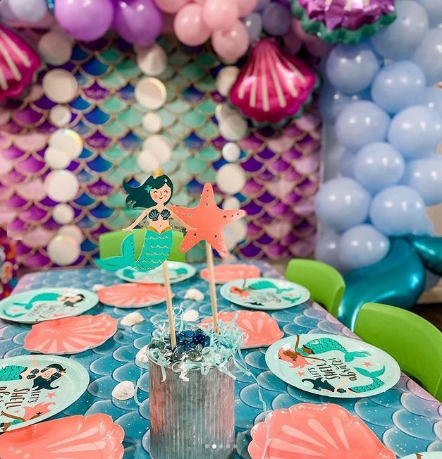 A table set for a mermaid birthday party with plates and balloons.