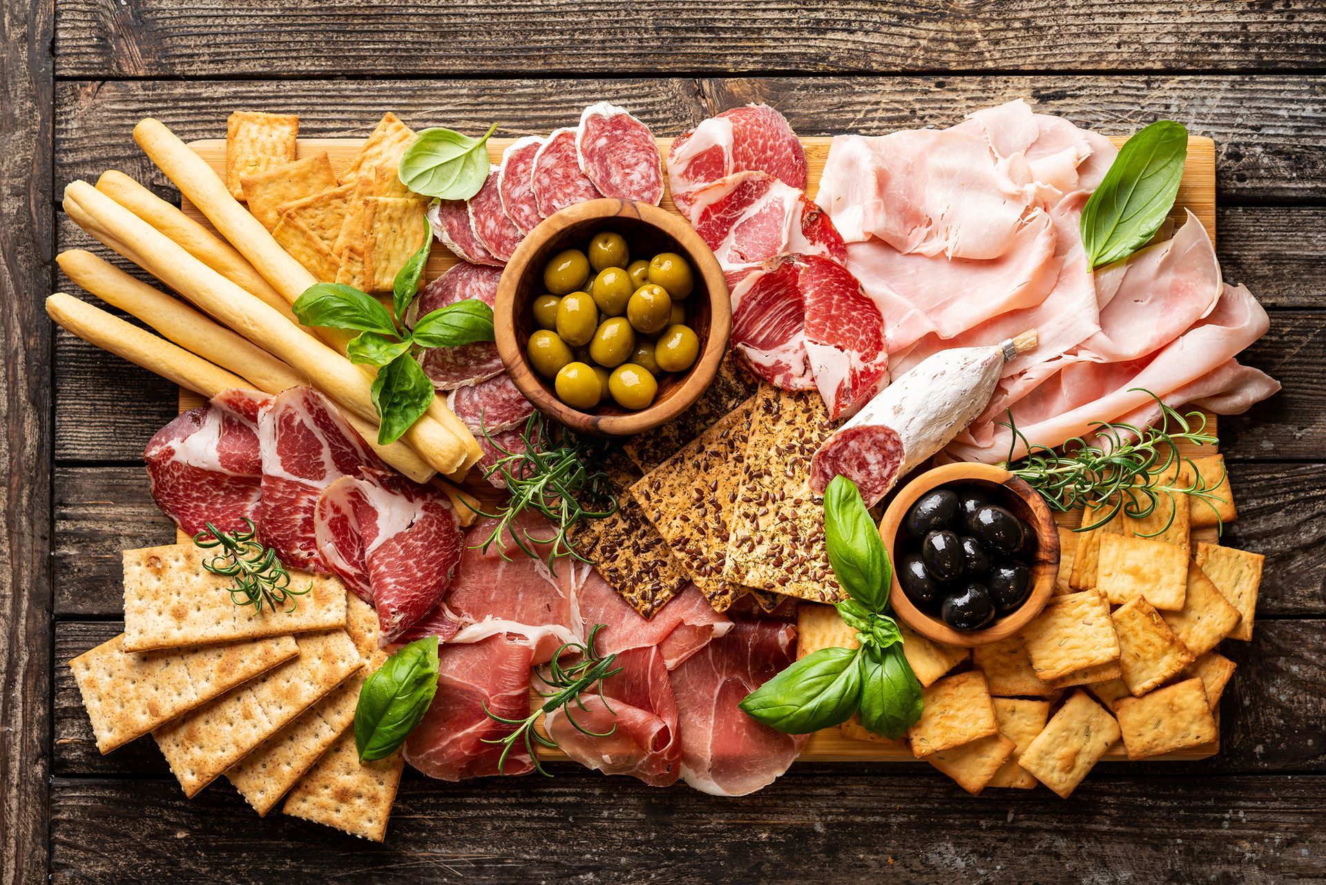 A wooden cutting board topped with a variety of meats and crackers.