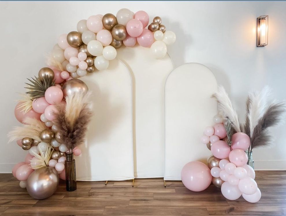 A room decorated with pink and gold balloons and pampas grass.