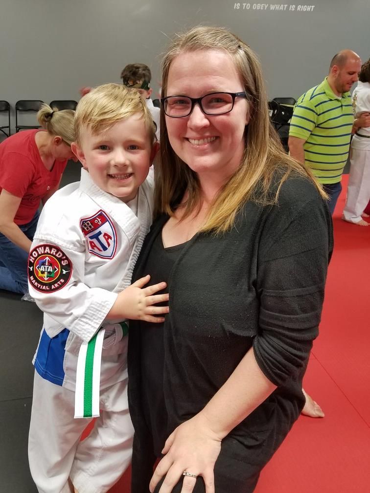 A woman is holding a young boy who is wearing a taekwondo uniform.