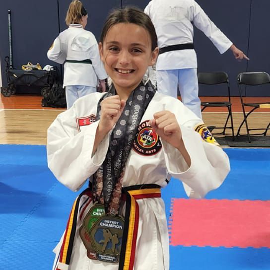 A young girl in a taekwondo uniform holds a medal around her neck