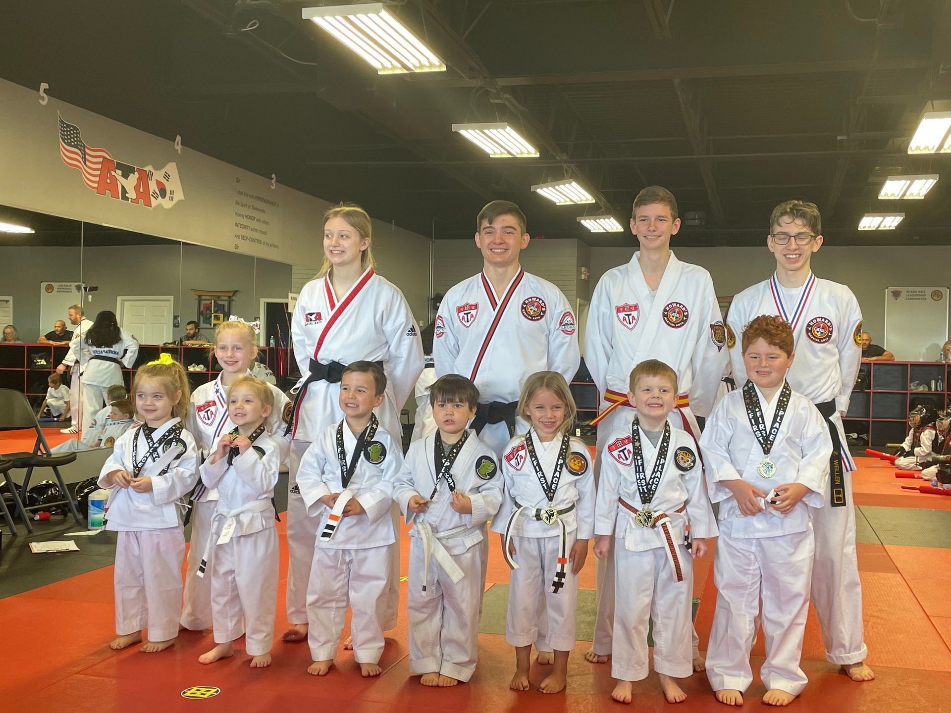 A group of children in karate uniforms are posing for a picture in a gym.
