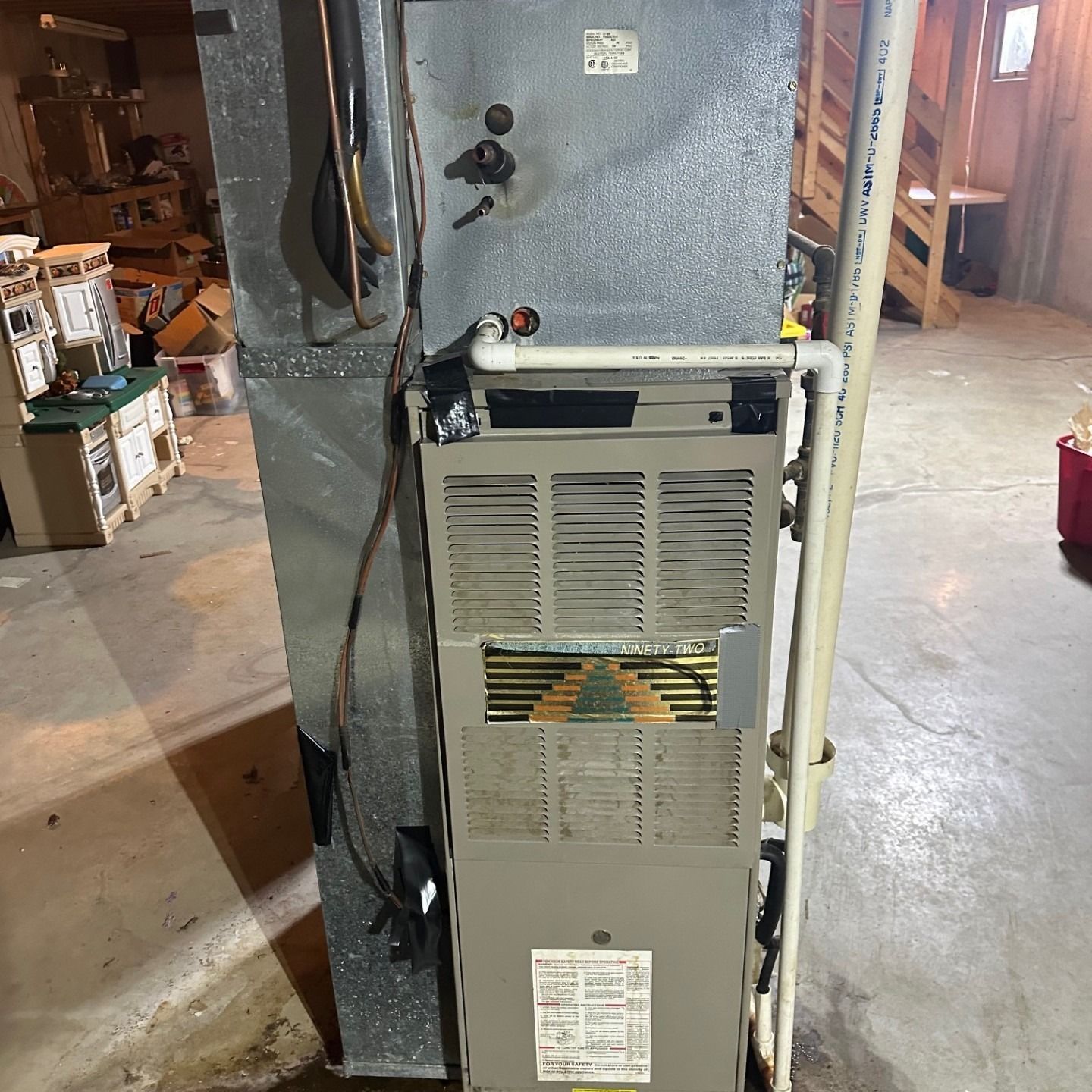 A furnace in a basement setting with ductwork and pipes.