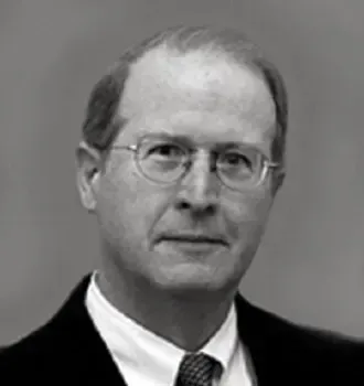 A man wearing glasses and a suit and tie is looking at the camera in a black and white photo.