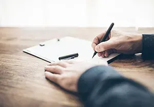 A person is writing on a clipboard with a pen.