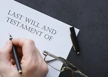 A person is writing a last will and testament on a piece of paper.