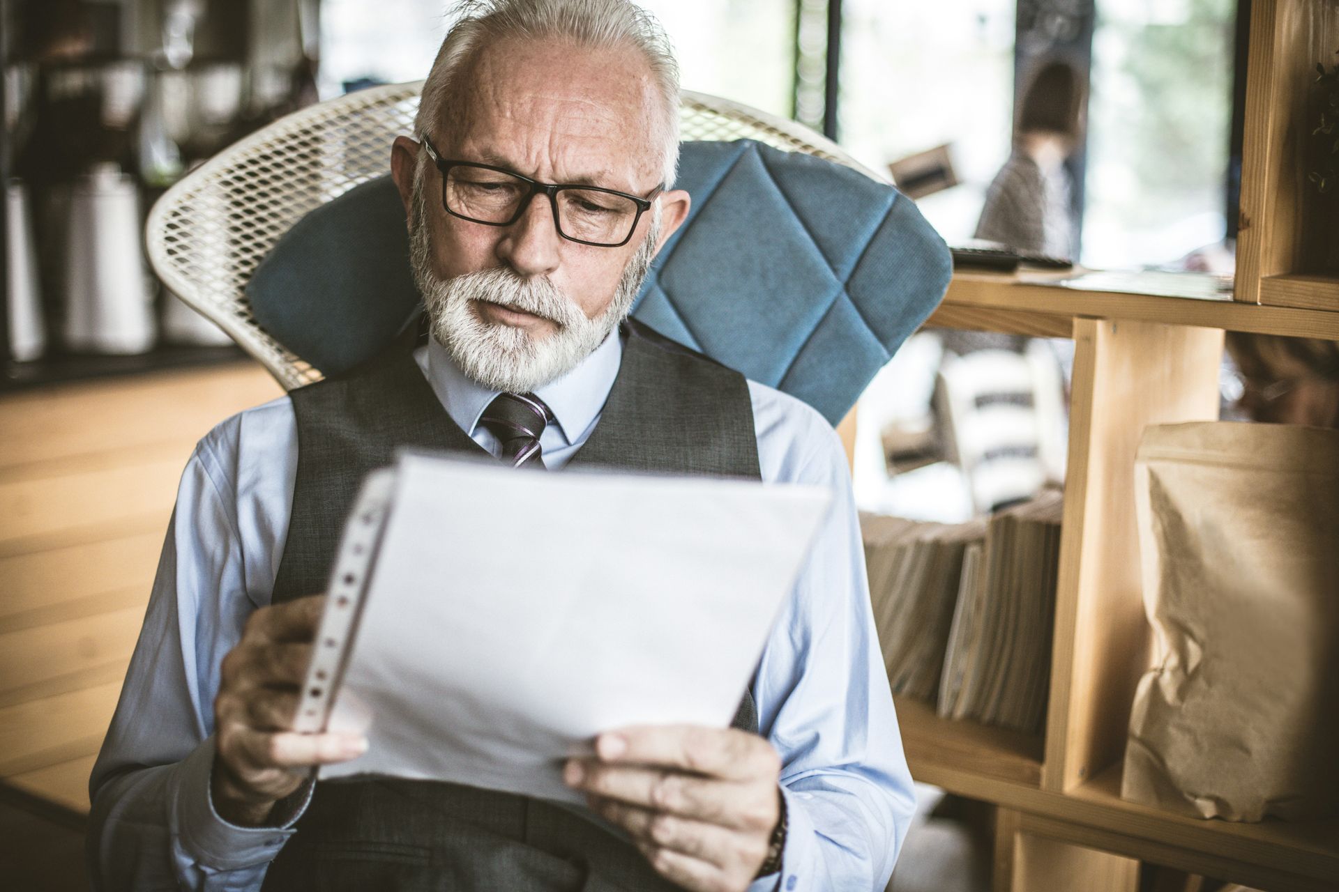 An older man is sitting in a chair reading a piece of paper.