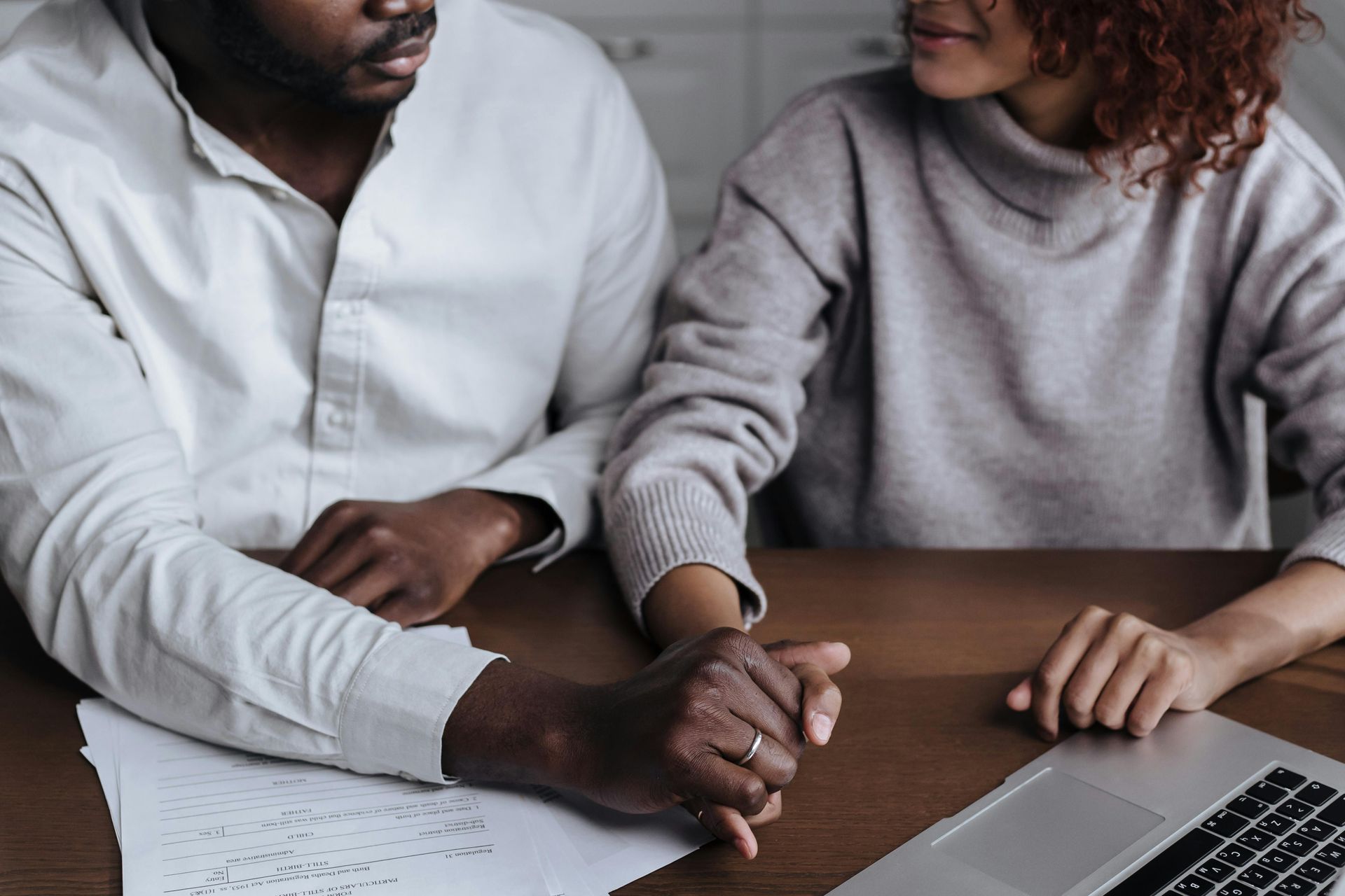 A man and a woman are holding hands while sitting at a table with a laptop.