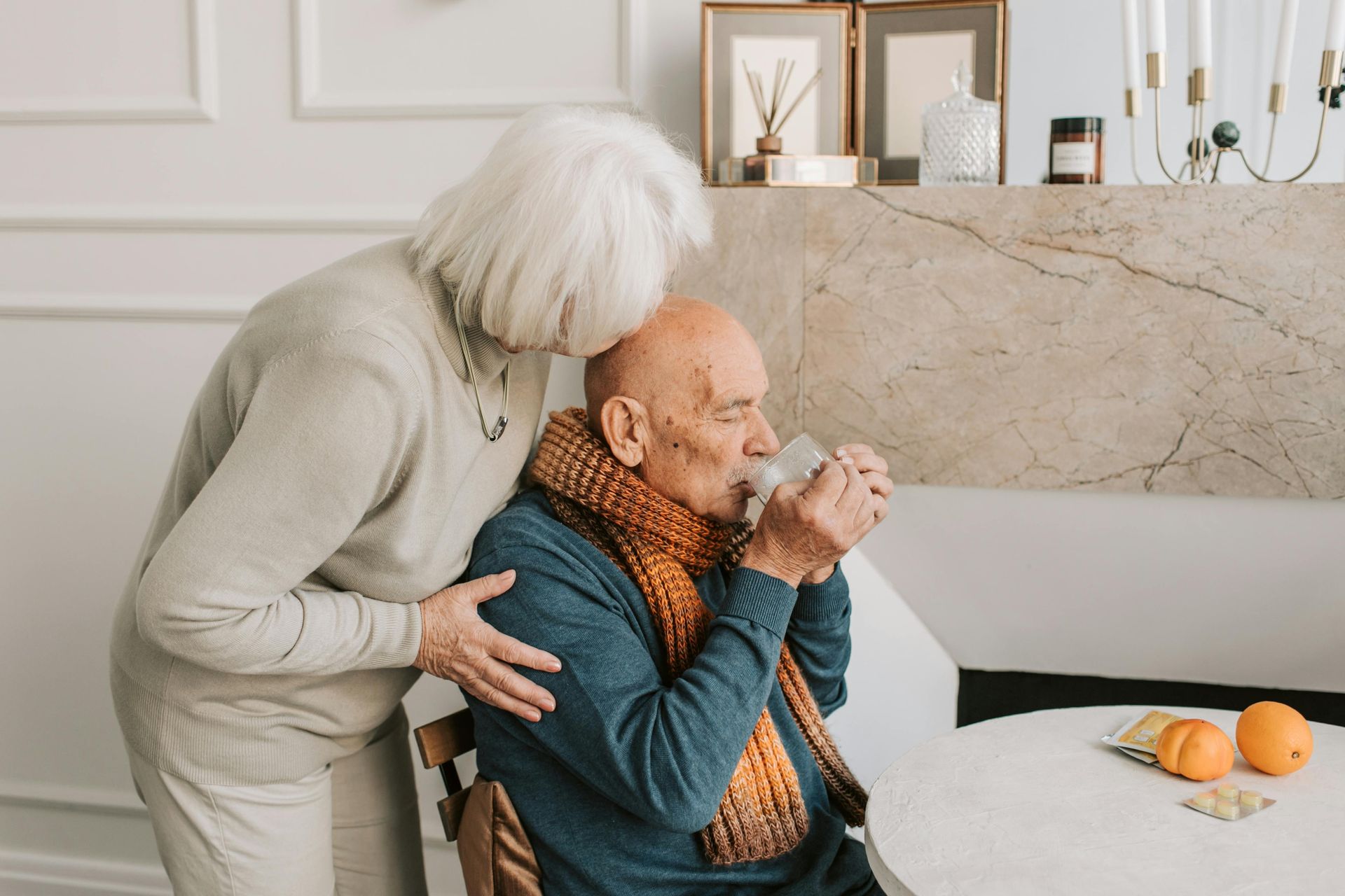 An elderly couple is sitting at a table drinking from a cup.