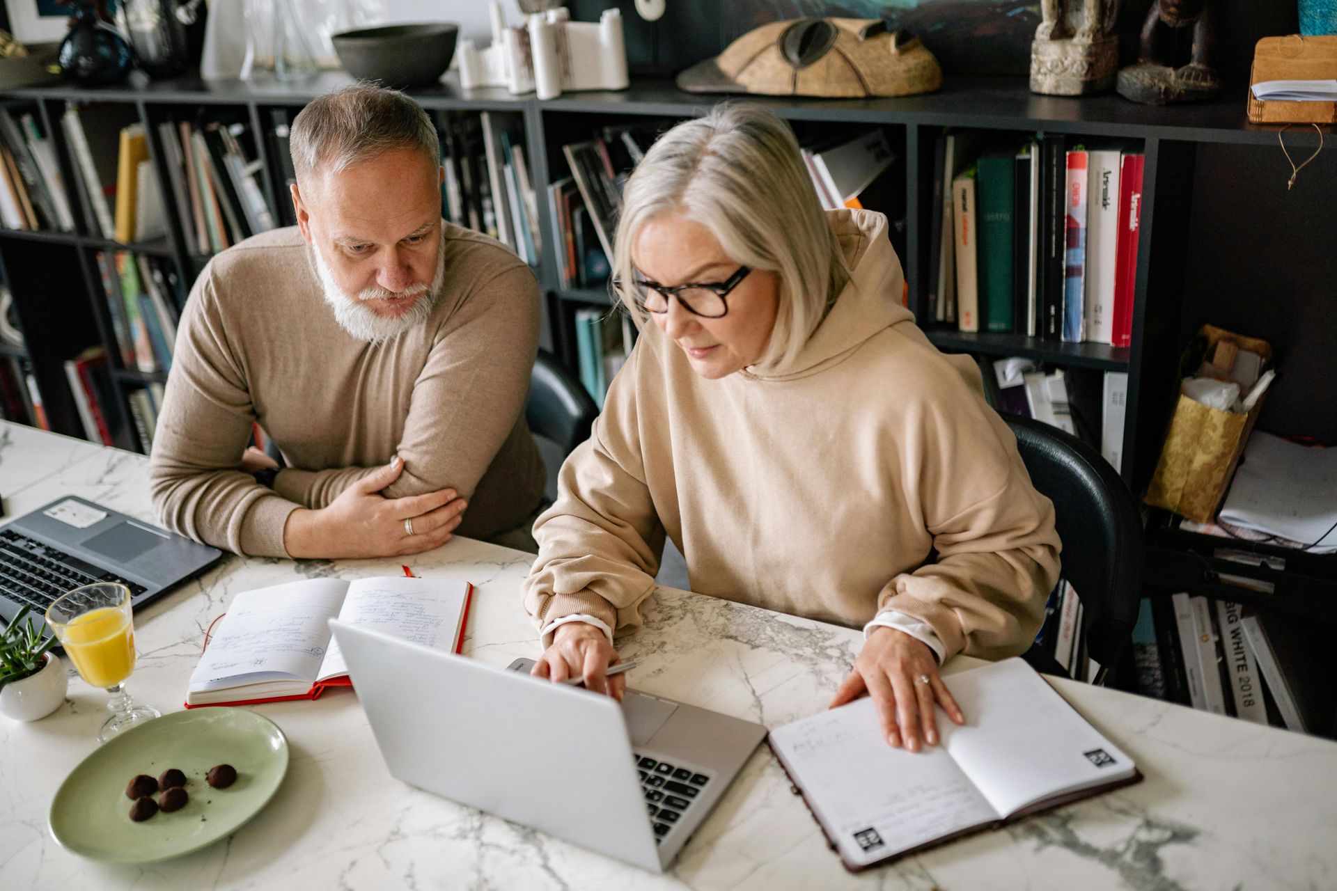 A man and a woman are sitting at a table looking at a laptop.