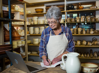 A woman is standing in front of a laptop computer in a pottery shop.