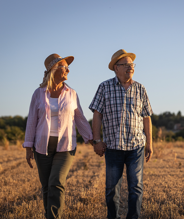 A man and a woman are walking through a field holding hands.