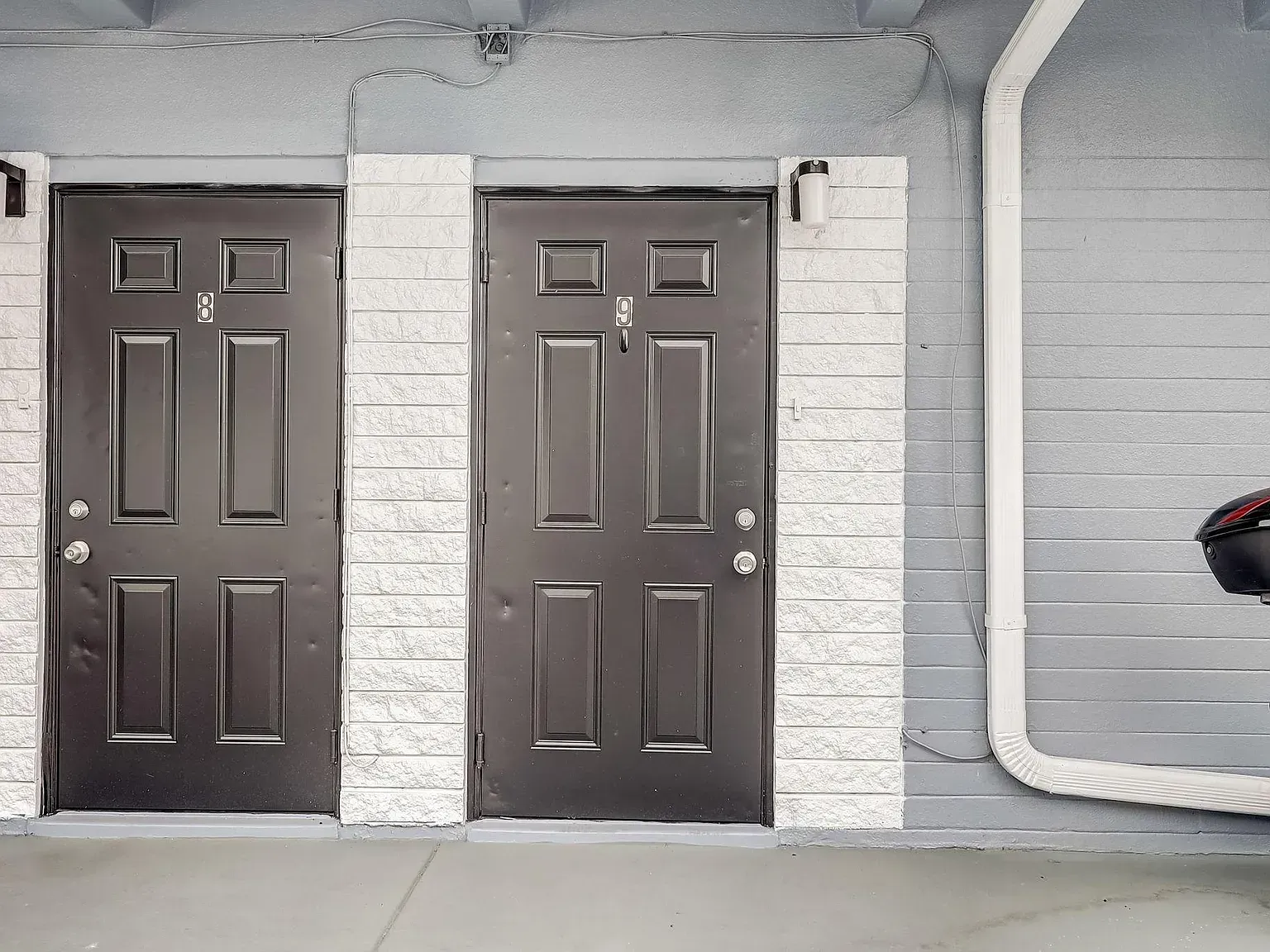 Two black doors with white trim on a gray building. A white gutter is visible on the right.