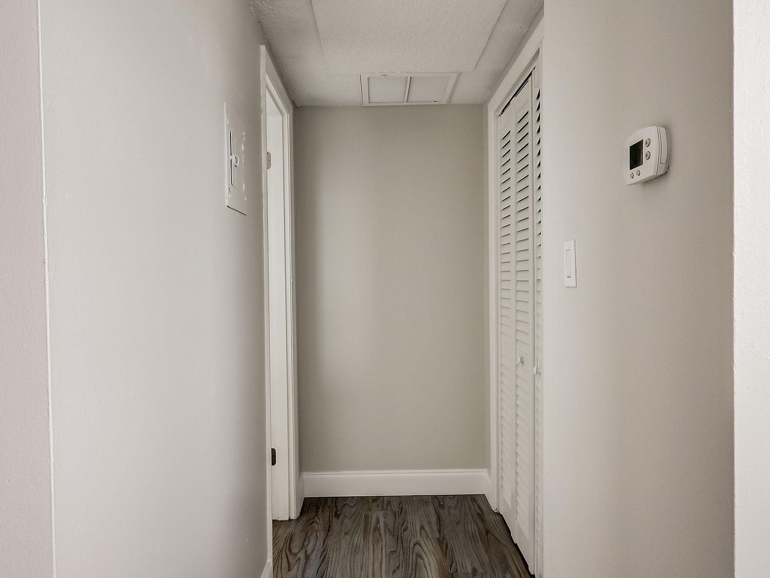 Narrow hallway with light gray walls, dark wood-look floor, and white doors.