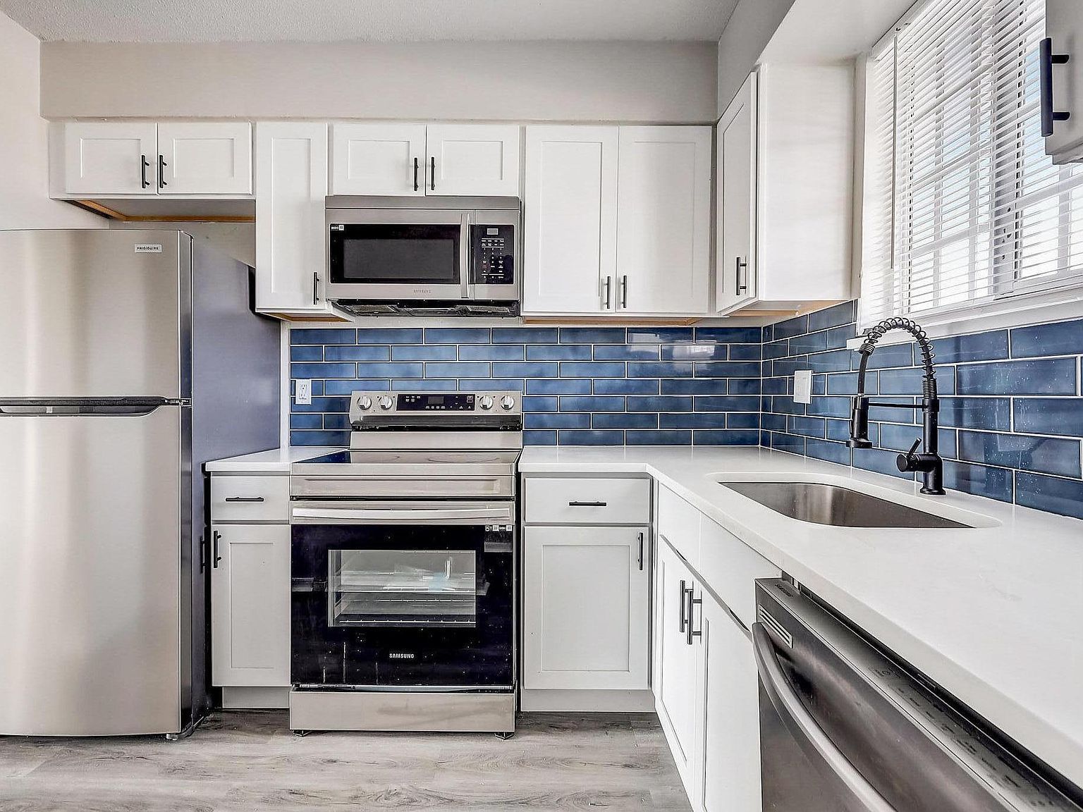 White kitchen with stainless steel appliances, blue tiled backsplash, and white countertops.