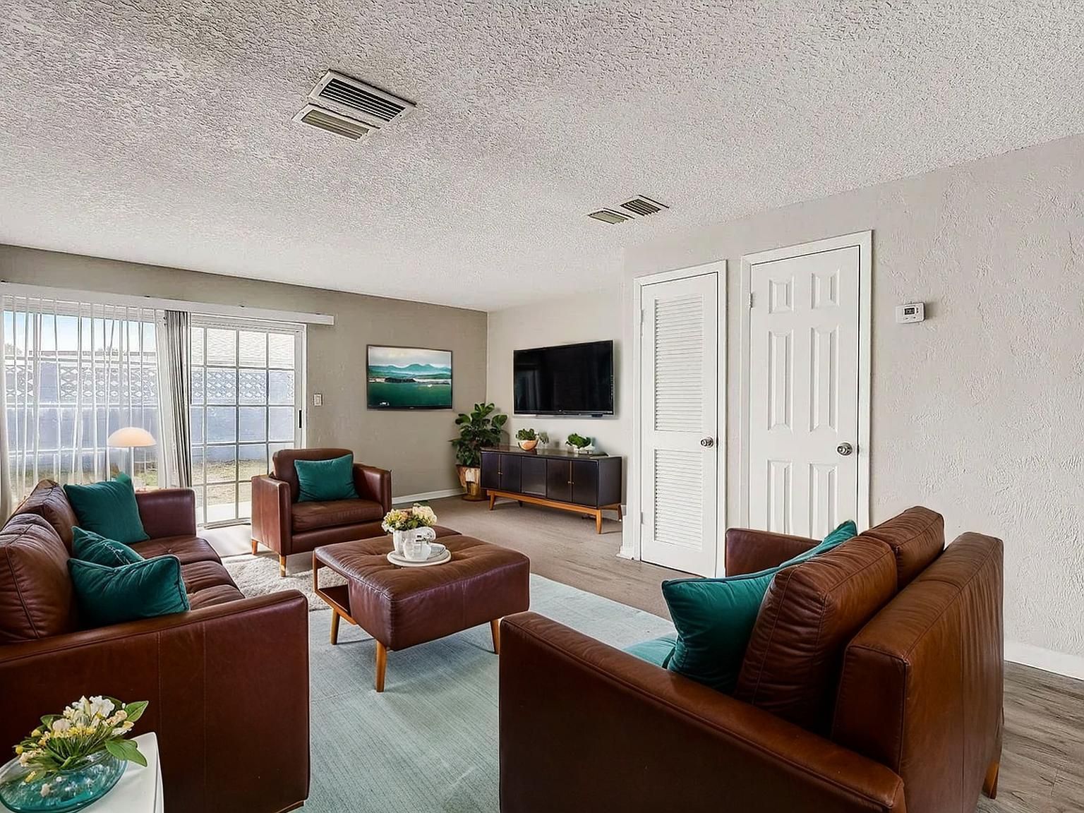 Living room with brown leather furniture, teal pillows, and a TV mounted on the wall.