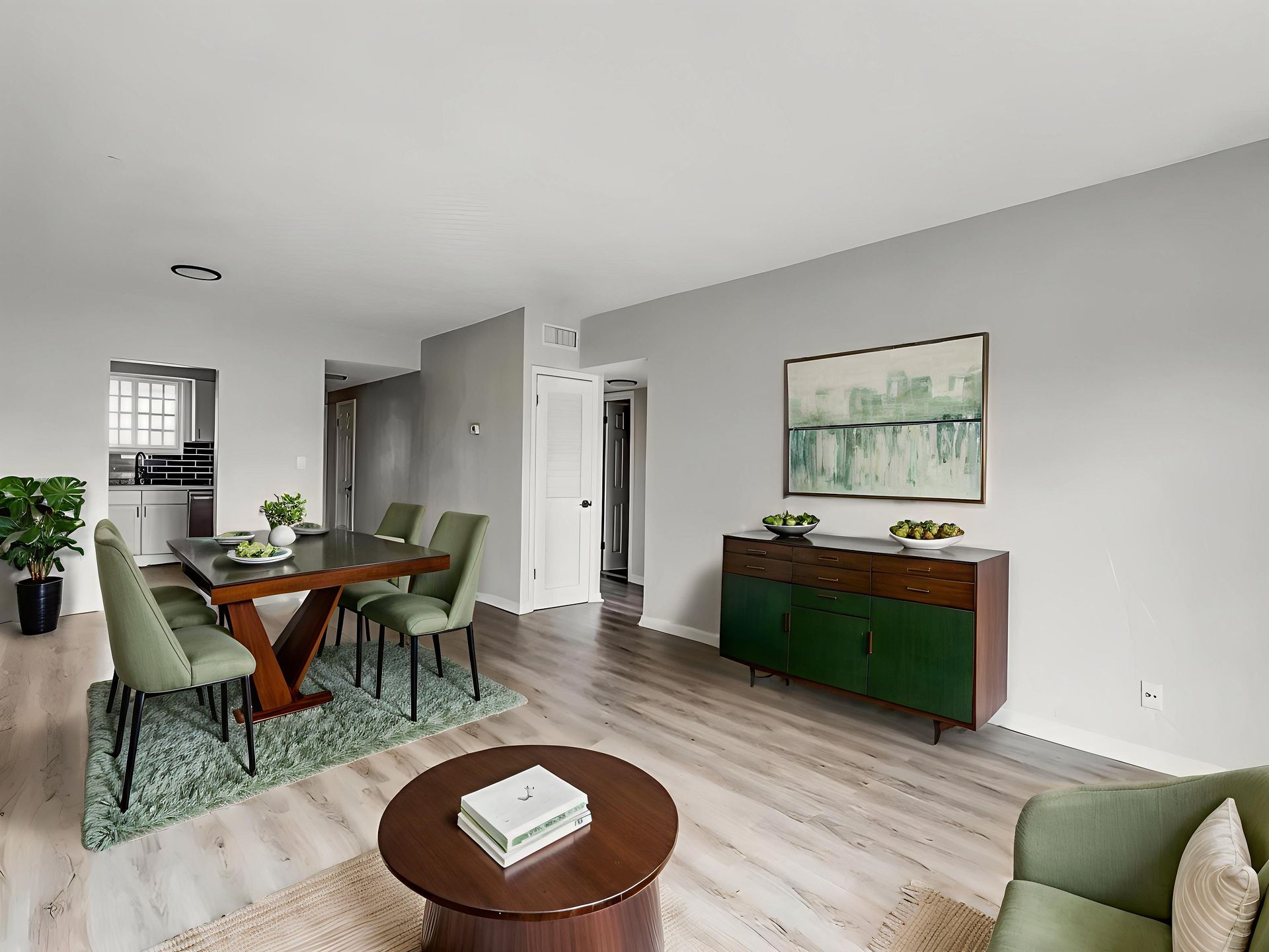 Dining room with table, chairs, sideboard, rug, and artwork. Grey walls, green and brown furniture.