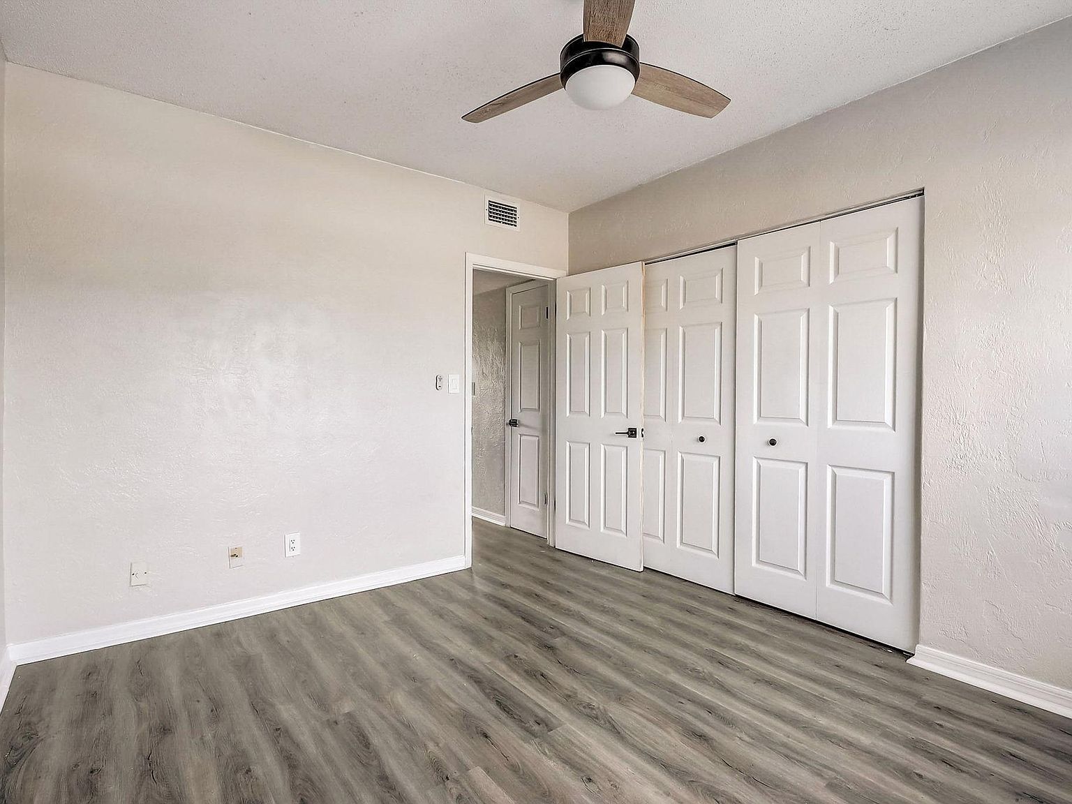 Empty bedroom with gray wood-look flooring, white closet doors, and a ceiling fan.