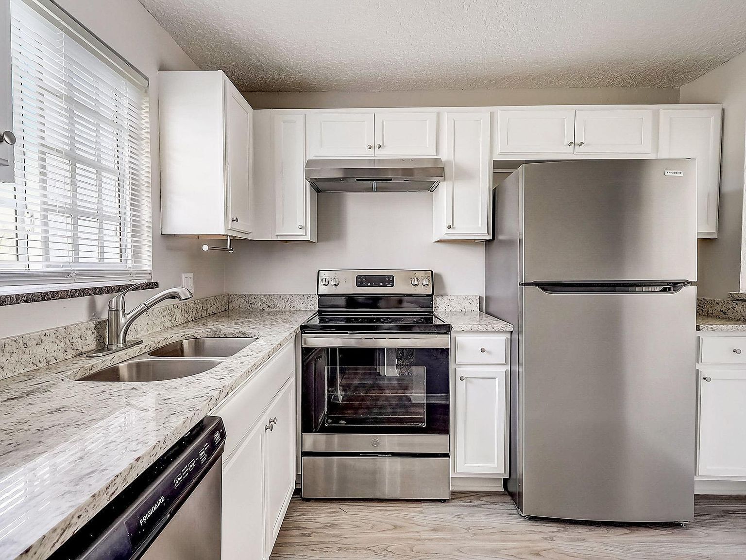 White kitchen with stainless steel appliances, granite countertops, and a window.