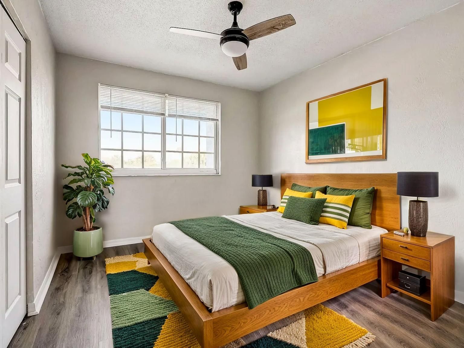 Bedroom with a bed, nightstands, artwork, rug, and ceiling fan in shades of green, yellow, and wood tones.