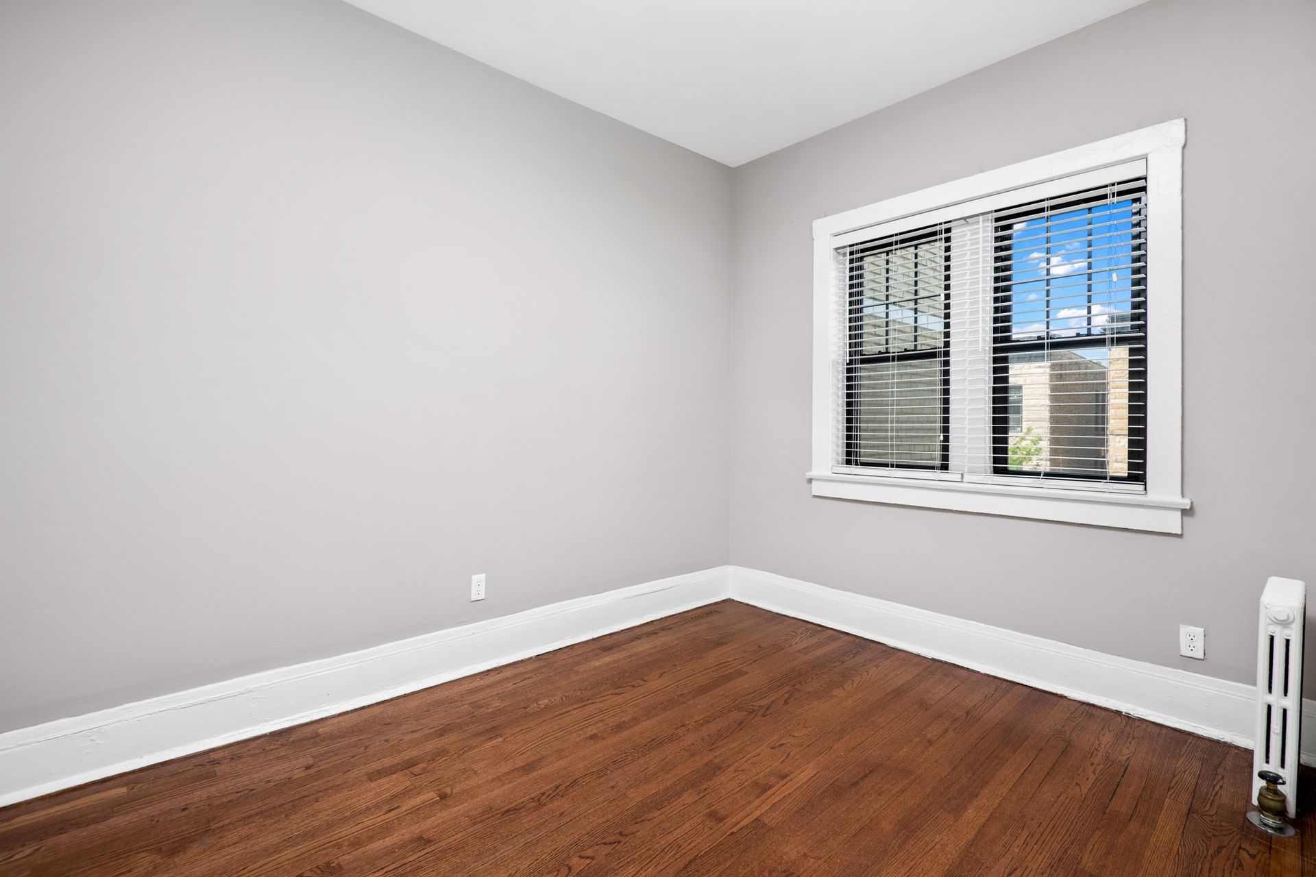 An empty room with hardwood floors and two windows at Irving Courts by Reside.