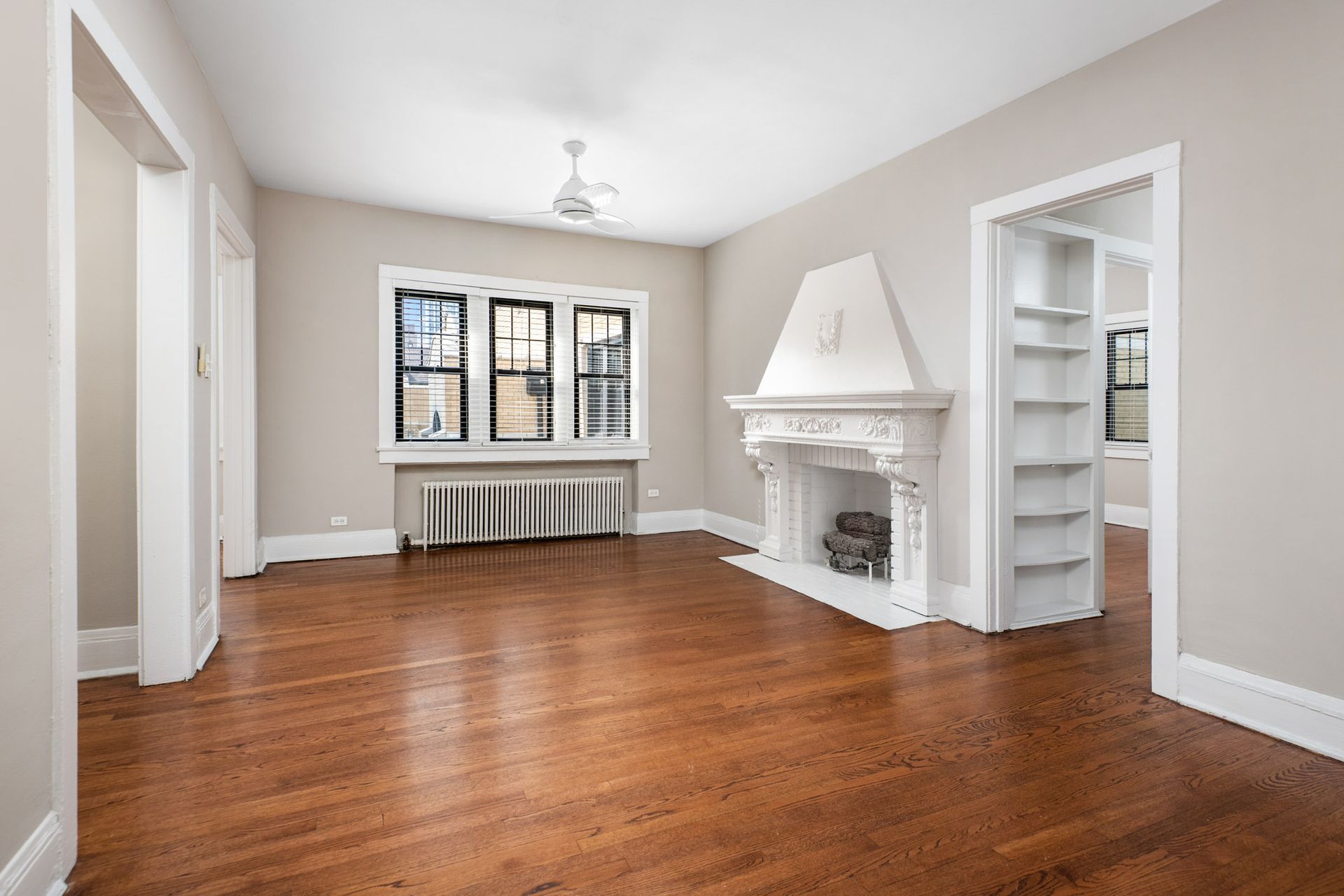 An empty living room with hardwood floors, windows, and a fireplace.