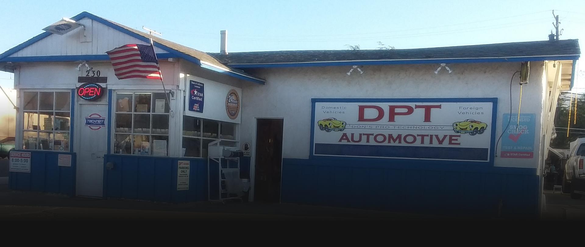 Exterior of DPT Automotive with an American flag. Blue and white building with a sign.