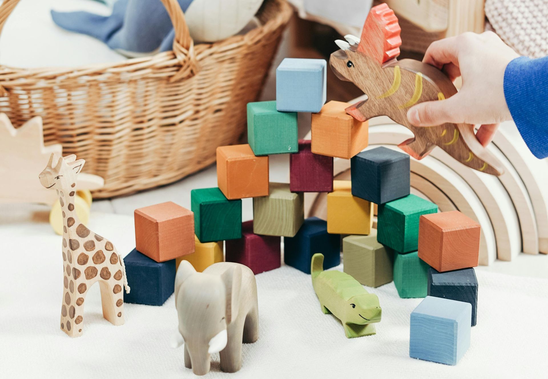 Multi coloured blocks stacked like a pyramid with a wooden toy giraffe, wooden toy elephant and wooden toy dinosaur next to it