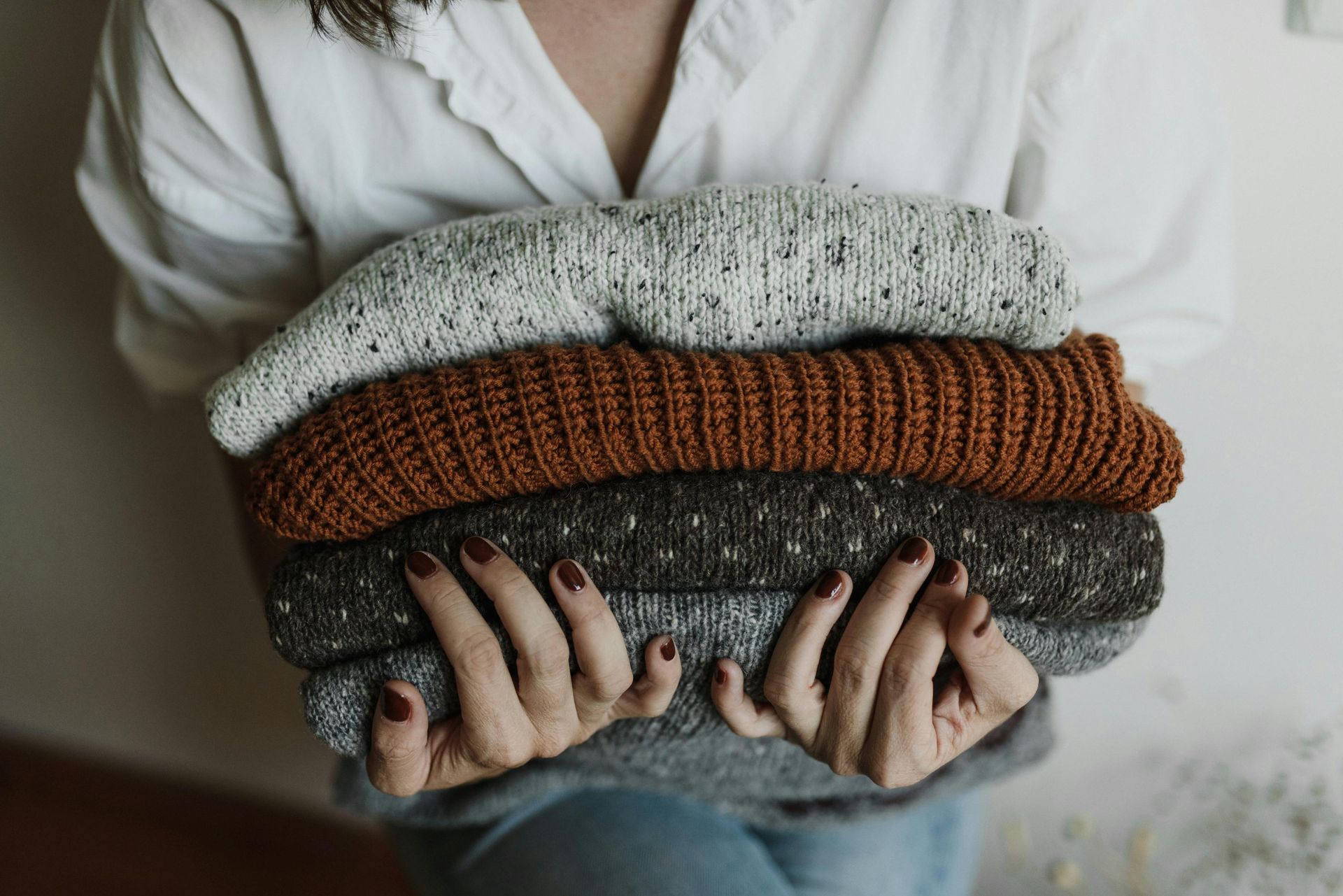 woman holding 4 folded wool knit jumpers