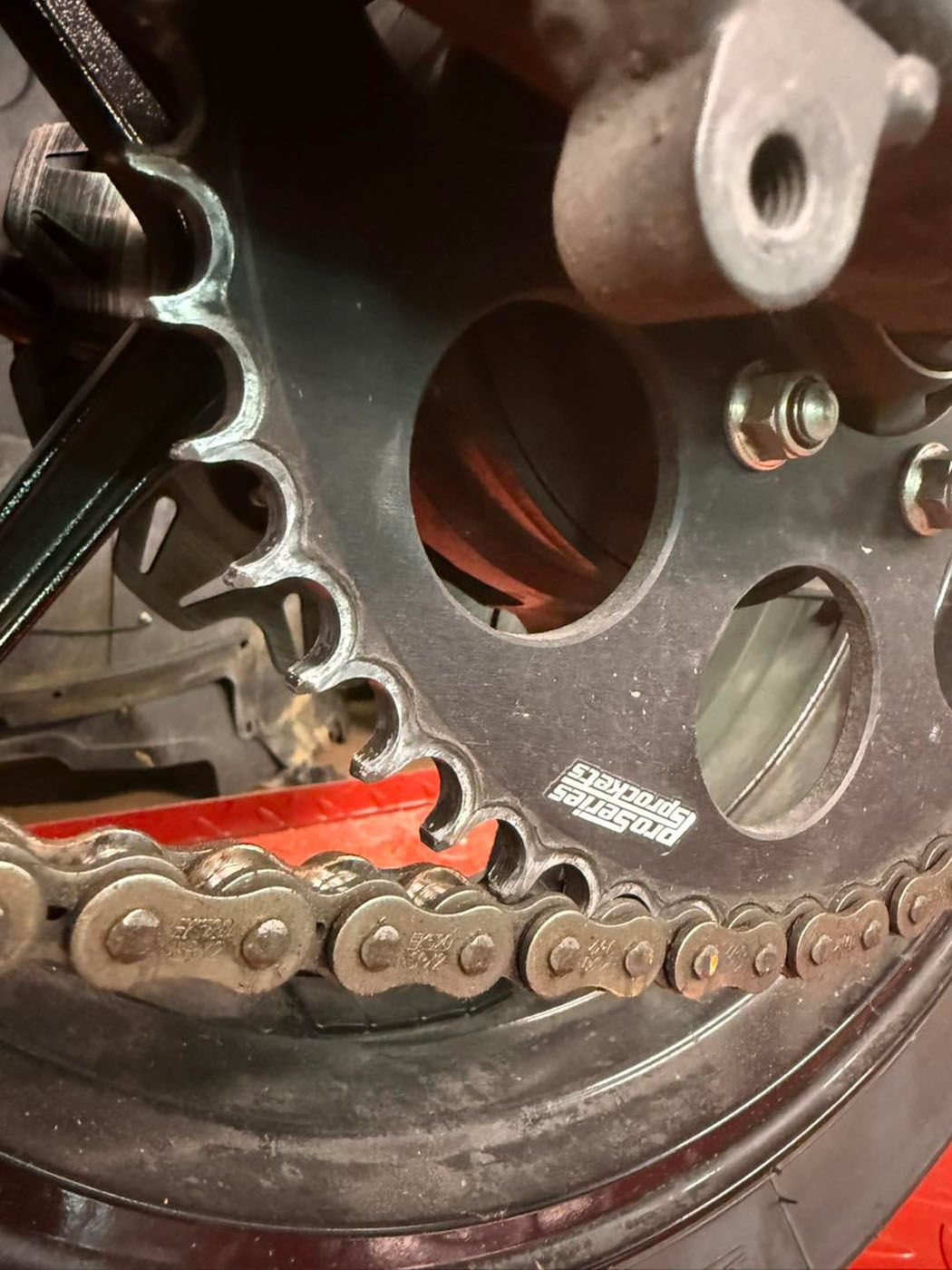 Close-up of a motorcycle chain and sprocket with a red chain guard.