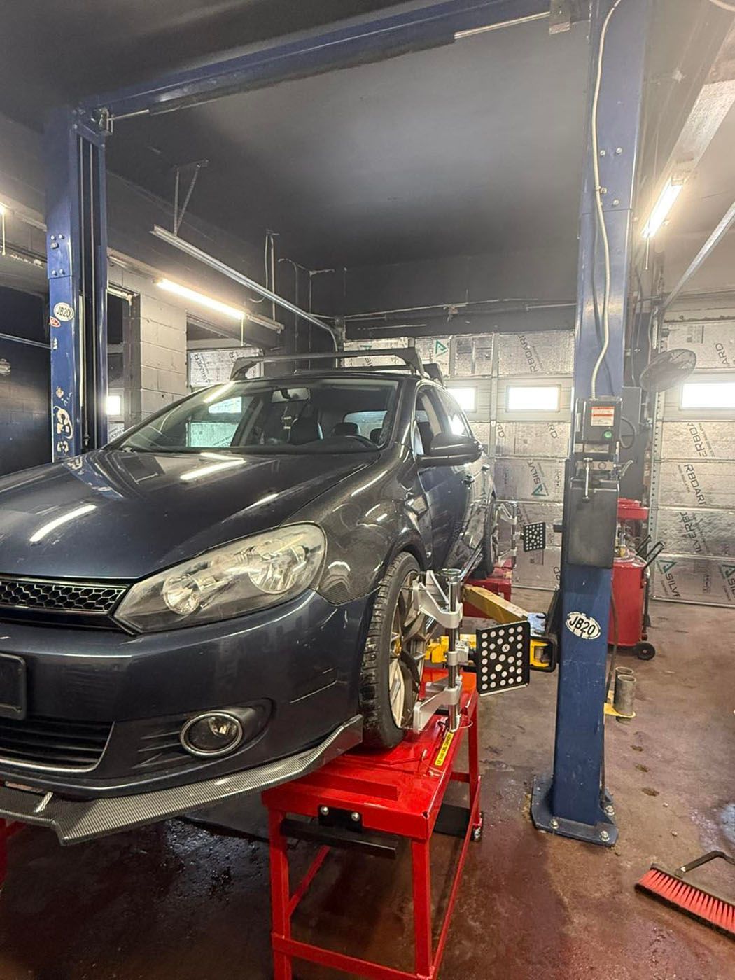 Dark blue sedan on a lift in an auto repair shop, with tools and equipment around it.