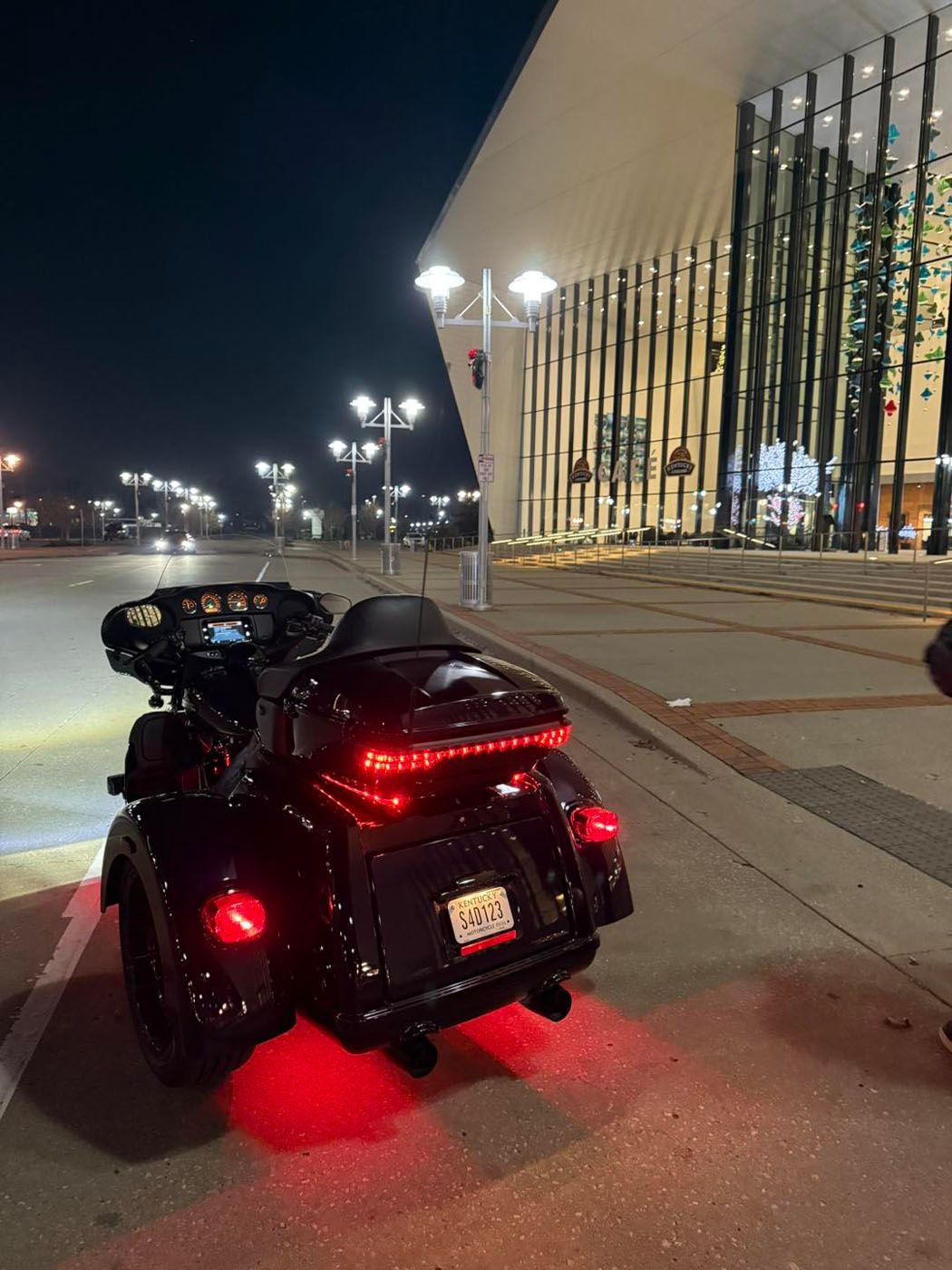Black motorcycle with red underglow parked at night beside a lit building.