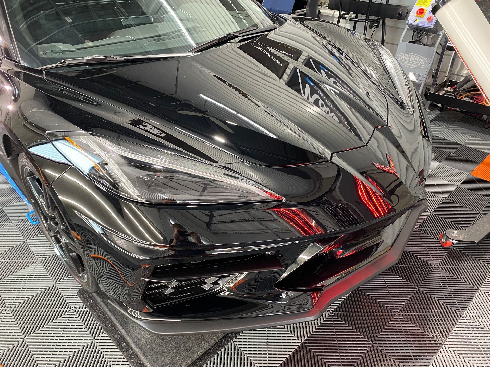 A black sports car is parked on a tiled floor in a garage.