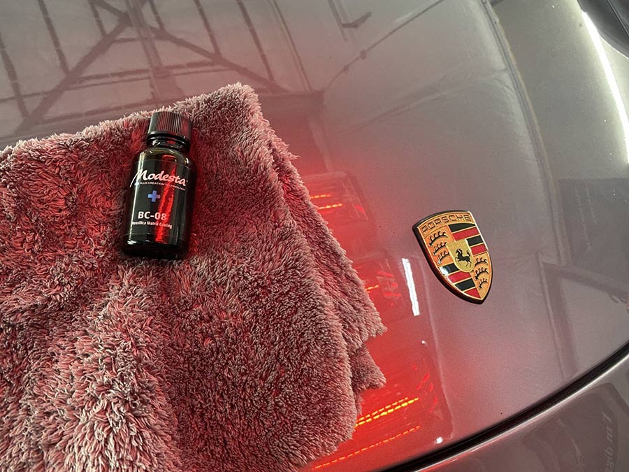A bottle of polish is sitting on a towel next to a porsche emblem.