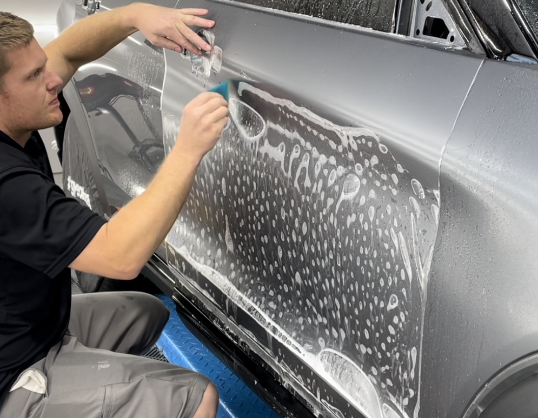 A man is applying a protective film to the side of a car.