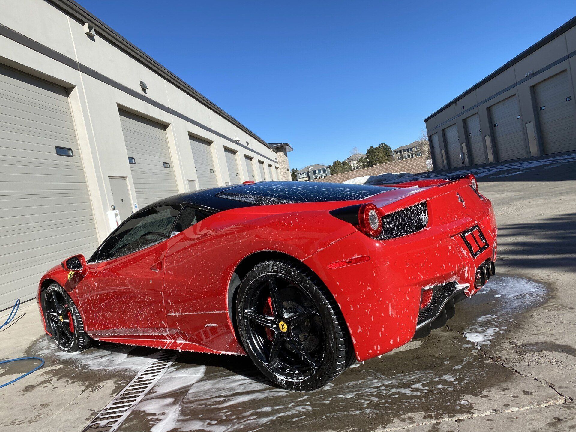 A red sports car is being washed in front of a building