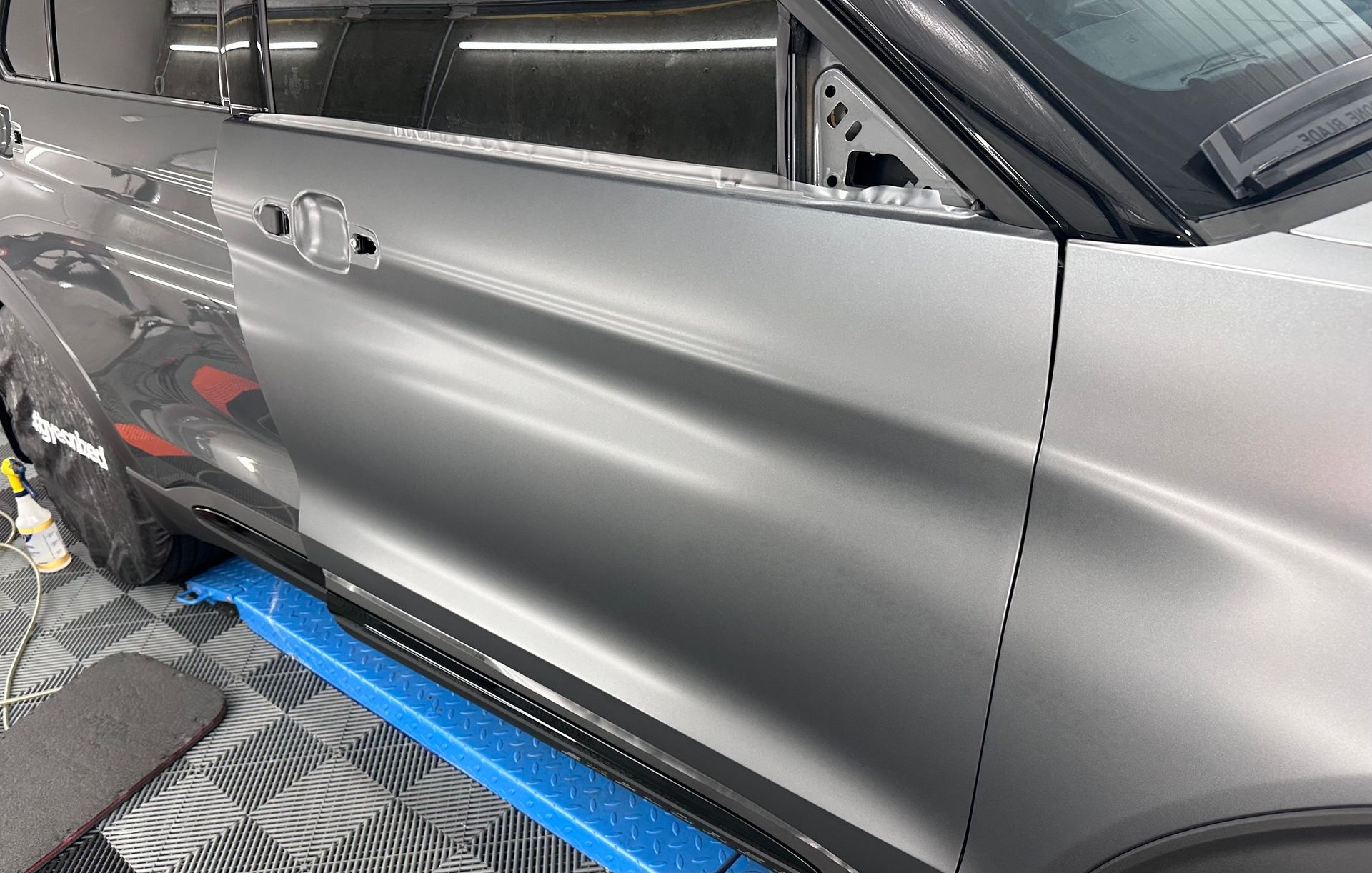 A gray car is sitting on top of a blue mat in a garage.