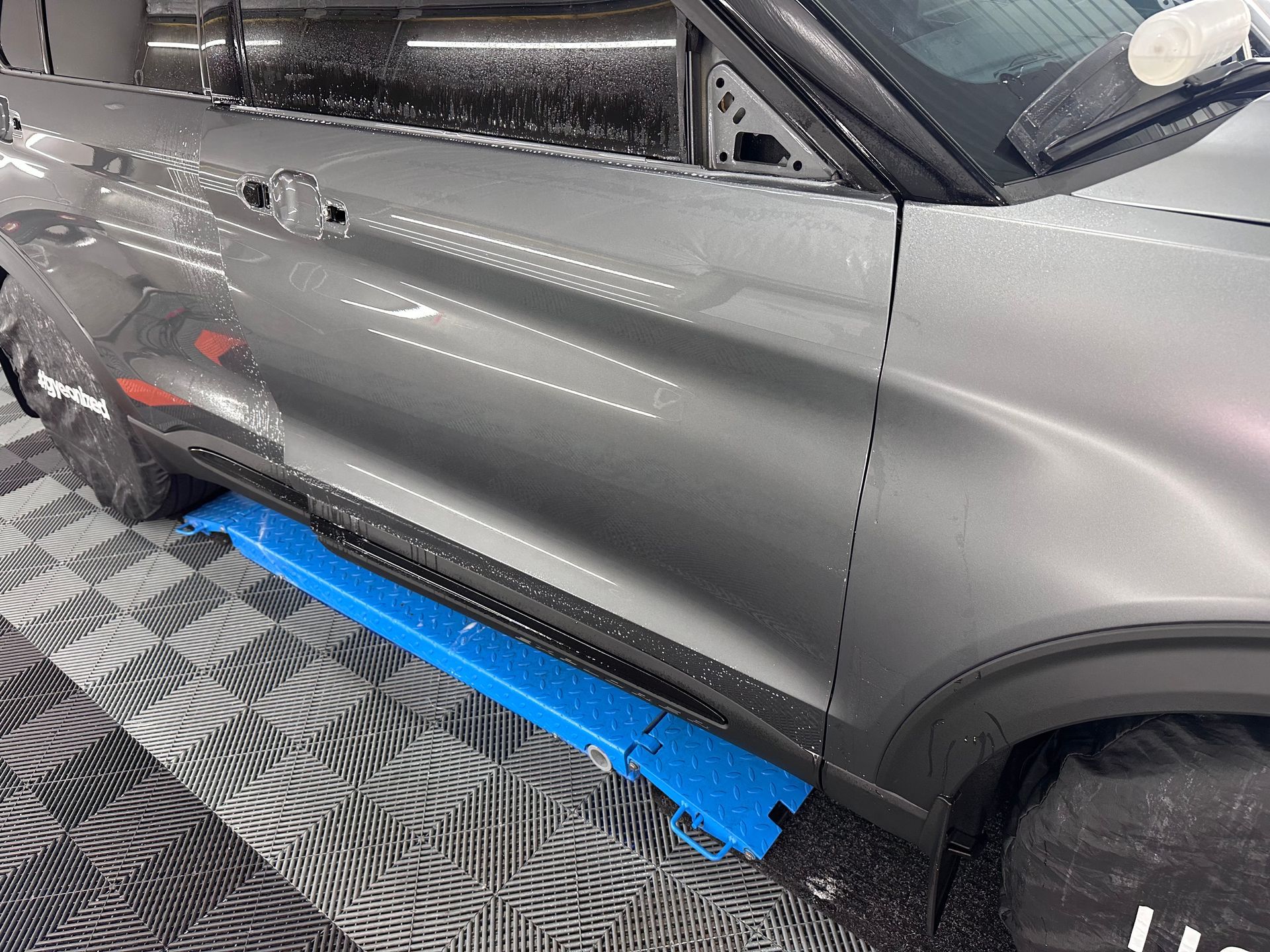 A gray car is parked on a checkered floor in a garage.