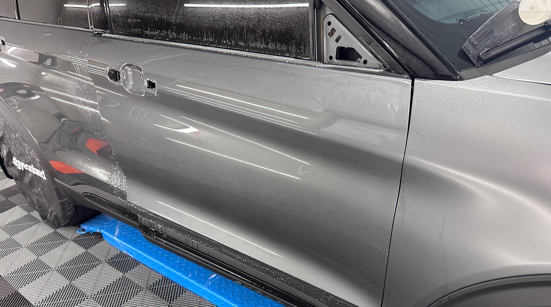 A gray car is parked on a checkered floor in a garage.