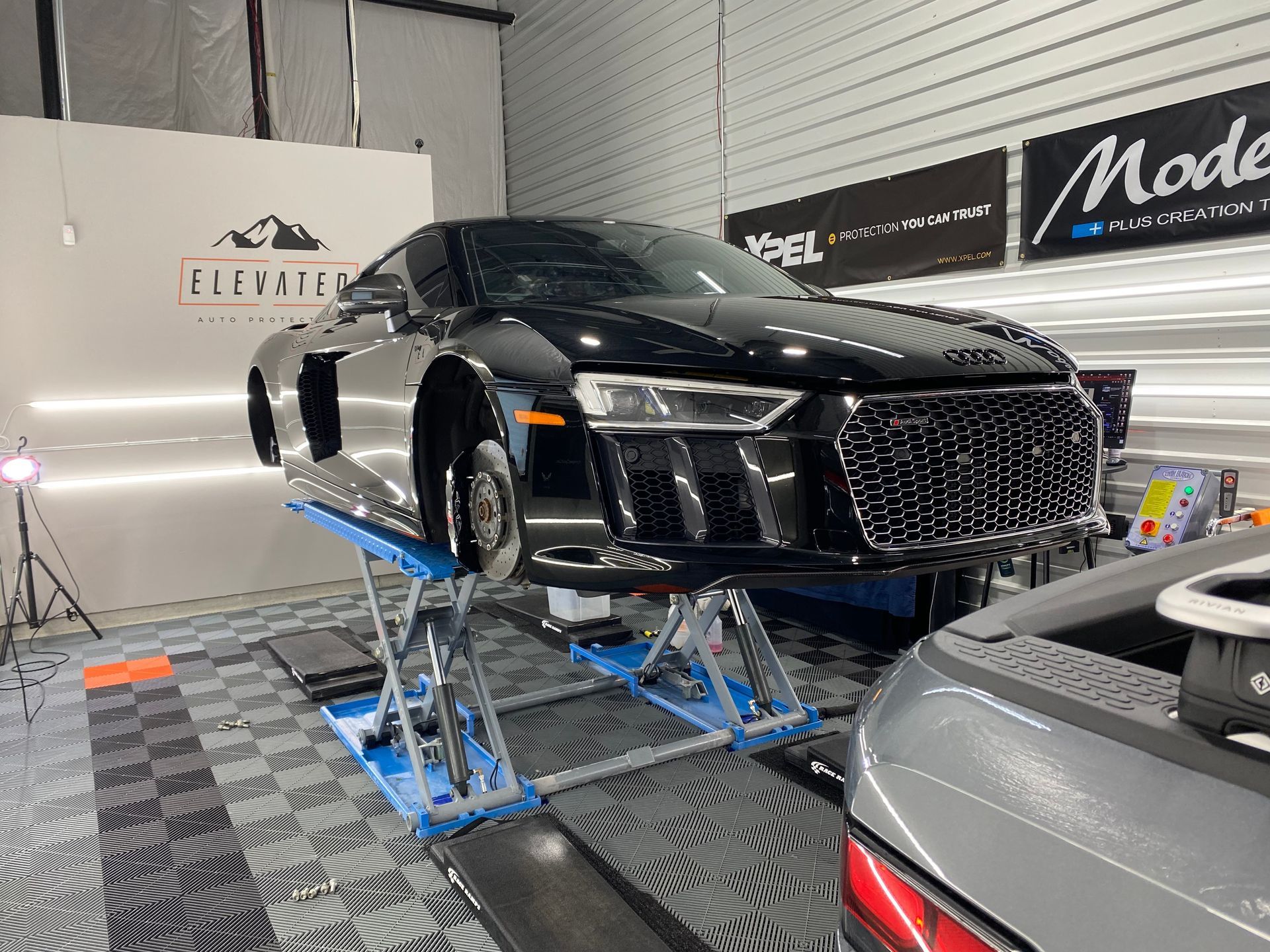 A black audi r8 is sitting on a lift in a garage.