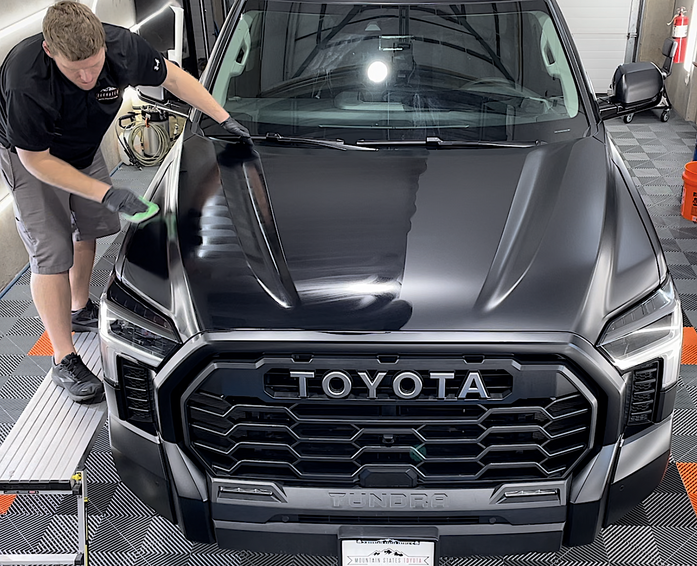 A man is polishing the hood of a black toyota truck.