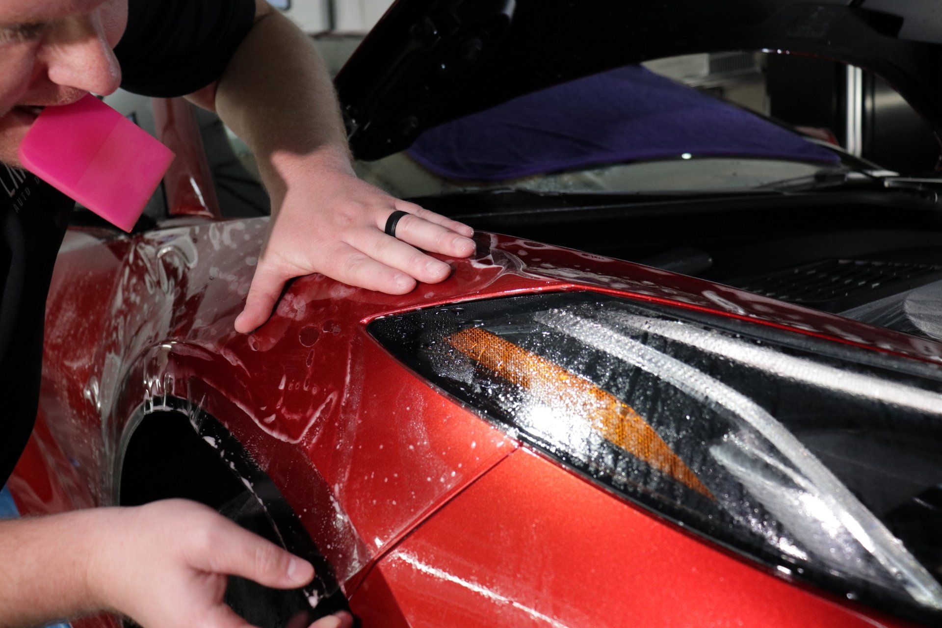 A man is wrapping a red car with plastic wrap.